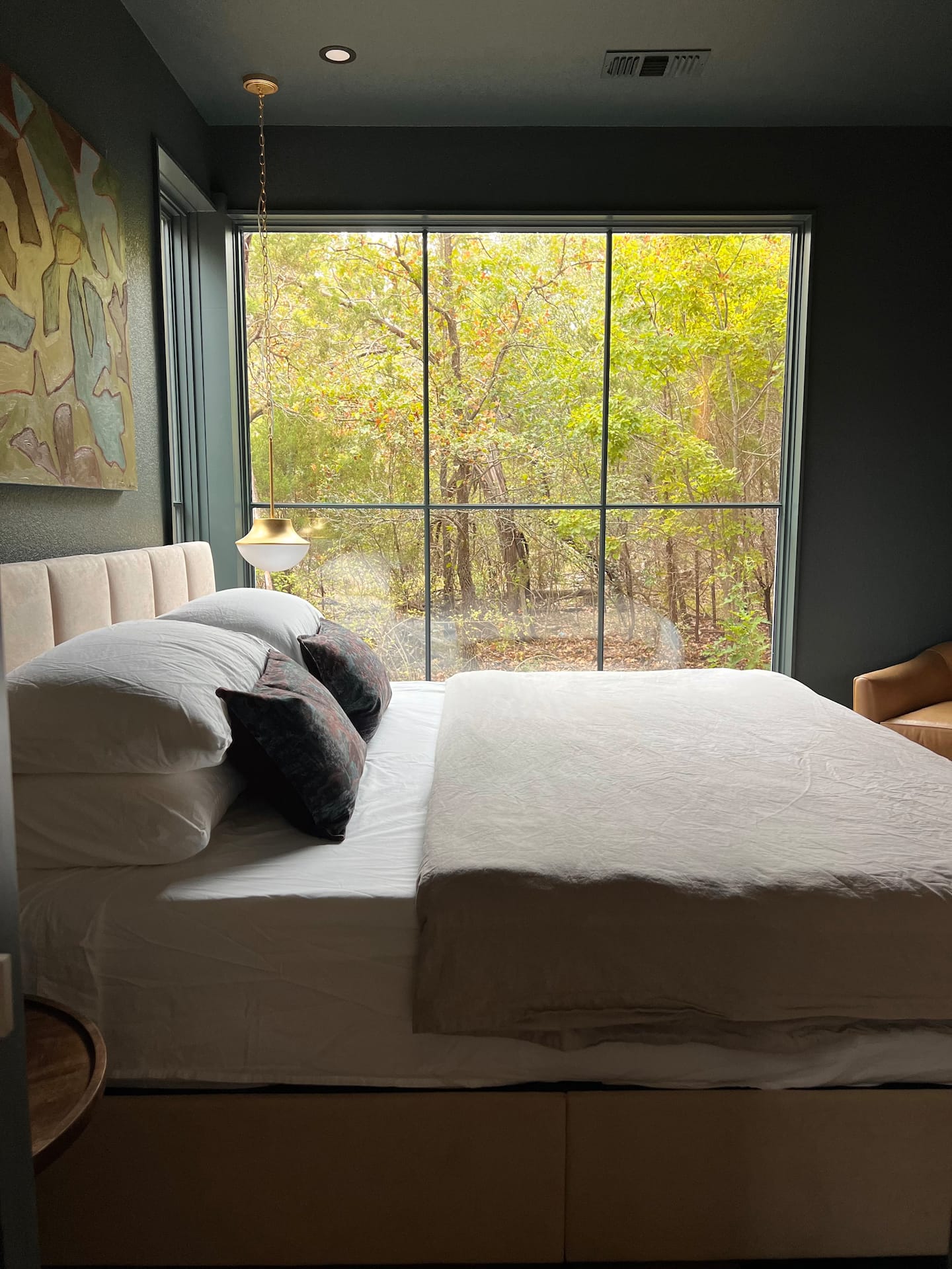 Primary suite with a king bed framed by a floor-to-ceiling forest window